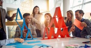 Diverse colleagues laugh and smile as they build two card towers, one red and one blue